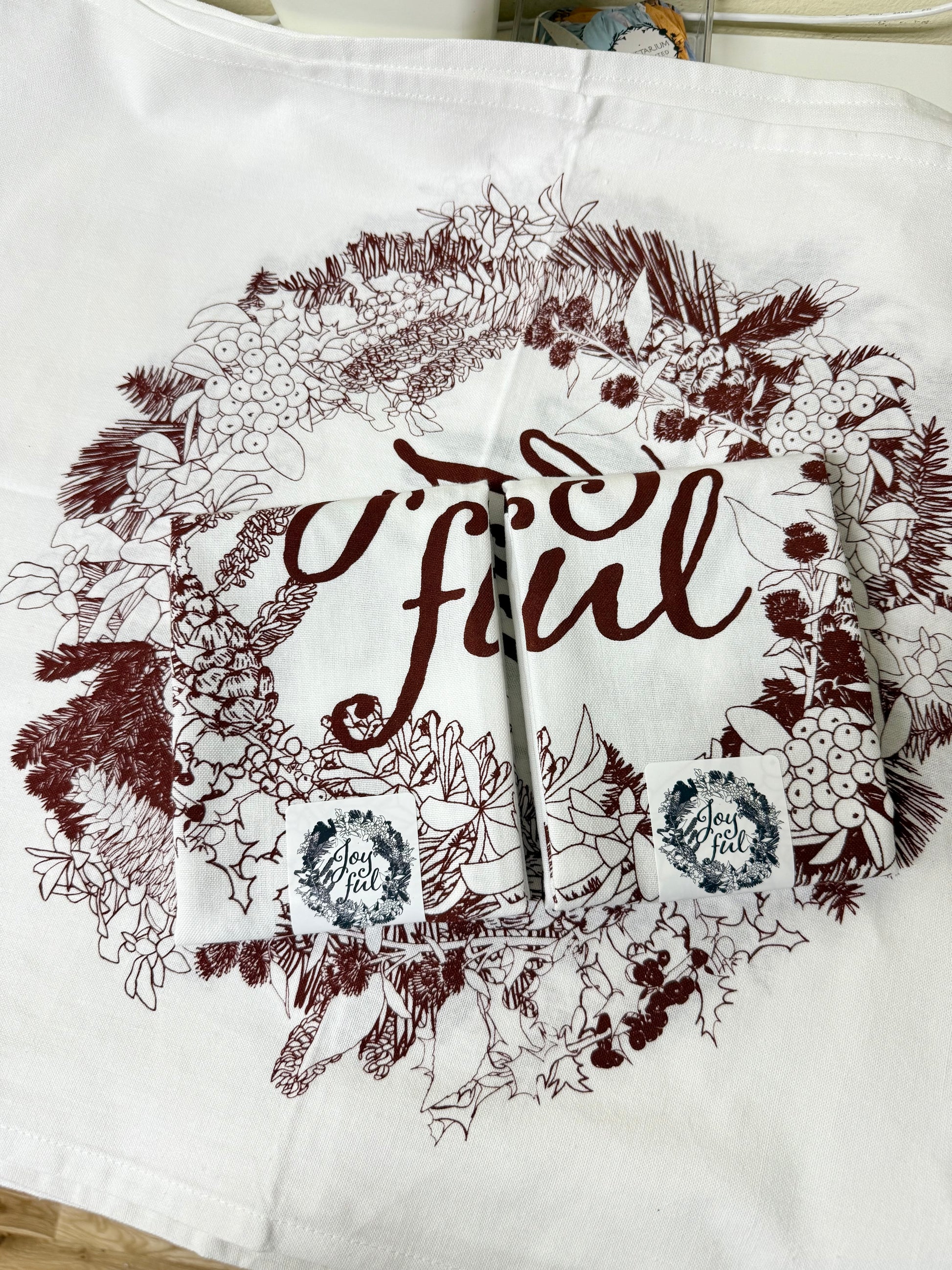 Hand-printed joyful holiday tea towel with festive botanical design