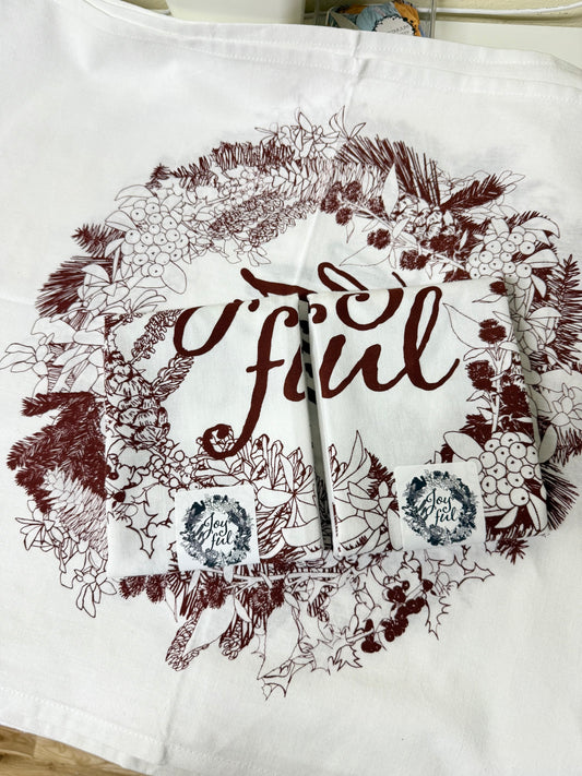 Hand-printed joyful holiday tea towel with festive botanical design