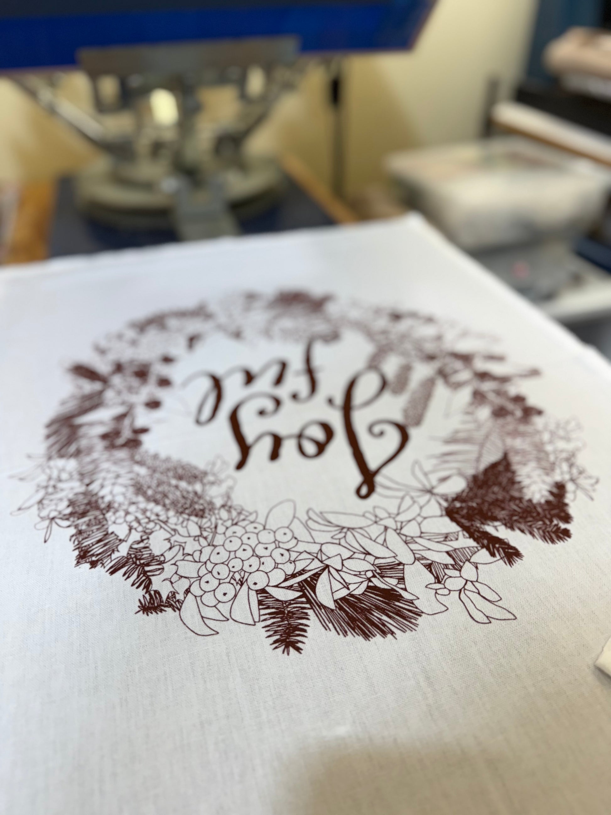 Hand-printed joyful holiday tea towel with festive botanical design